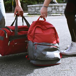 Two travelers holding red bags on a street, symbolizing travel and exploration.