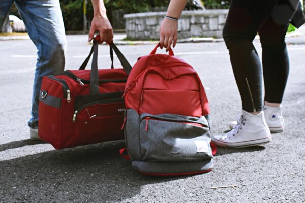 Two travelers holding red bags on a street, symbolizing travel and exploration.