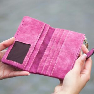 A woman holds an open, empty pink wallet outdoors, emphasizing financial themes.