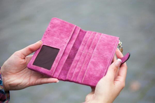 A woman holds an open, empty pink wallet outdoors, emphasizing financial themes.