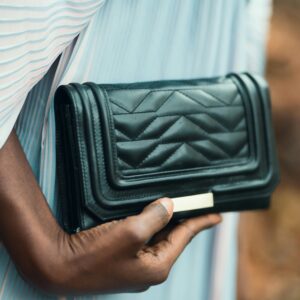 Close-up of a stylish black purse held by a person outdoors, showcasing elegance and fashion.