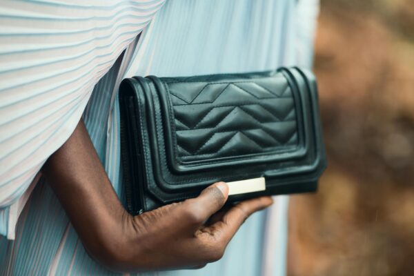 Close-up of a stylish black purse held by a person outdoors, showcasing elegance and fashion.